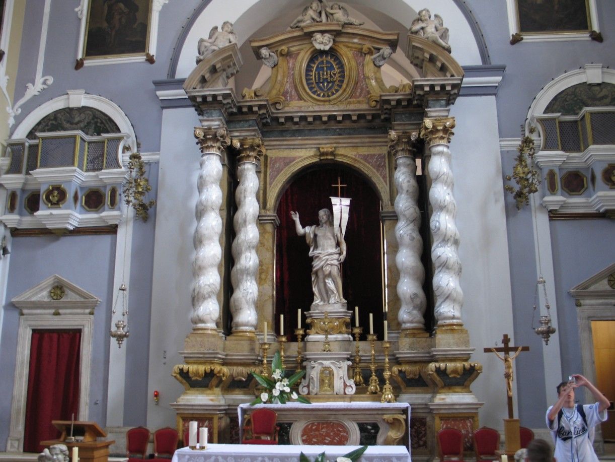 Altaar in een kerk. Een wit beeld staat in een nis, omlijst door spiraalvormige zuilen. 