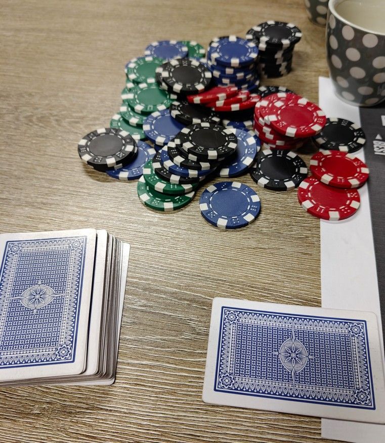 Een pak speelkaarten met blauwe achterkant ligt naast een stapel pokerfiches.