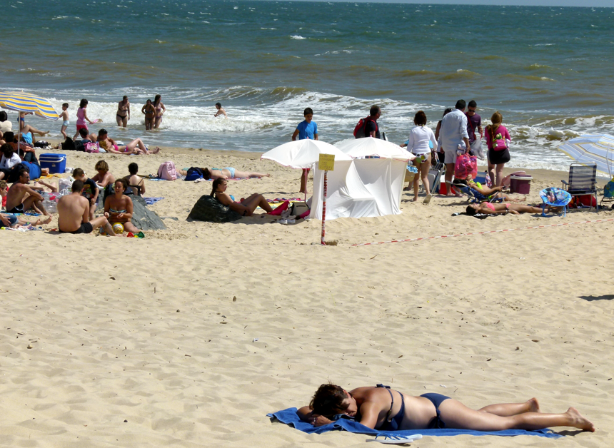 Strandtafereel met mensen die zonnebaden, zwemmen en bij het water staan. Wit zand, blauwe lucht en oceaan.