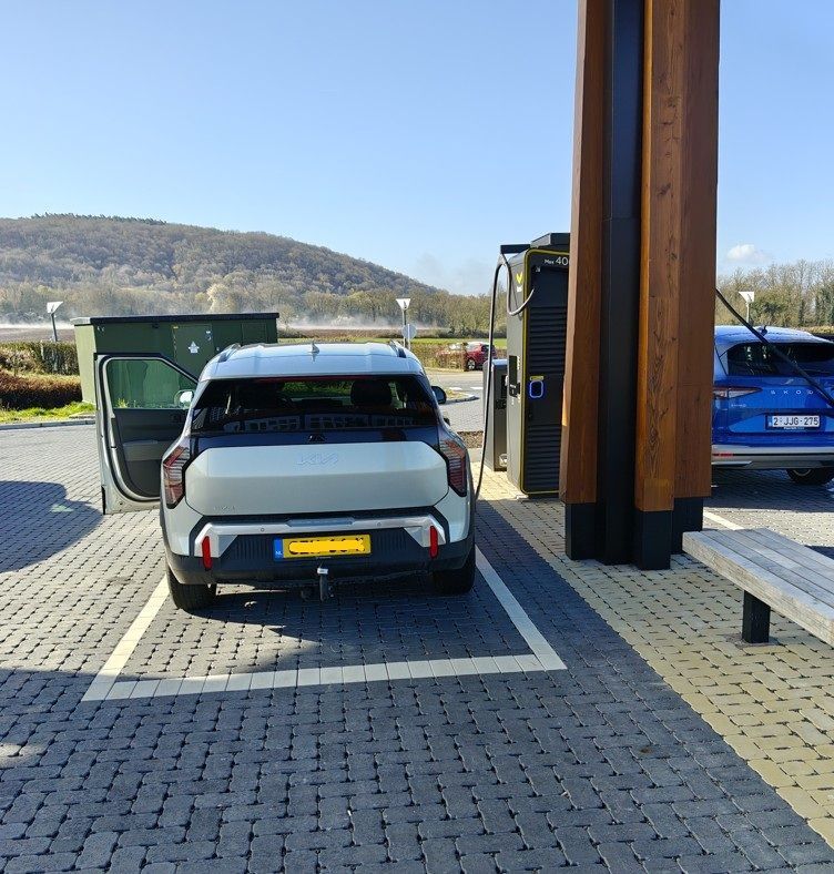 Een zilverkleurige auto geparkeerd bij een laadstation voor elektrische voertuigen op een verhard buitenterrein.