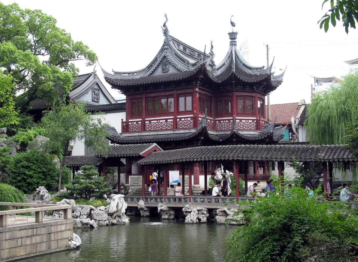 Traditioneel Chinees paviljoen met rode accenten en een donker pannendak, gelegen aan een meer met weelderig groen.