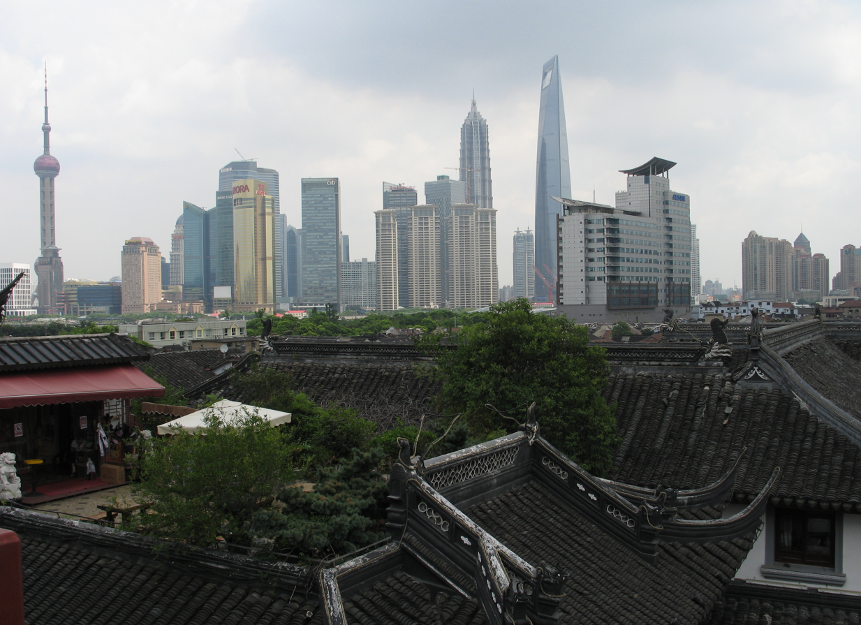 De skyline van Shanghai met traditionele daken op de voorgrond en wolkenkrabbers daarachter.