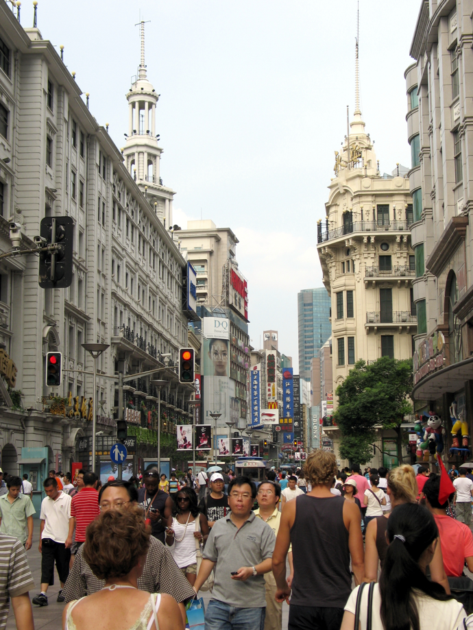 Een drukke straat in Shanghai met sierlijke gebouwen, verkeerslichten en voetgangers.