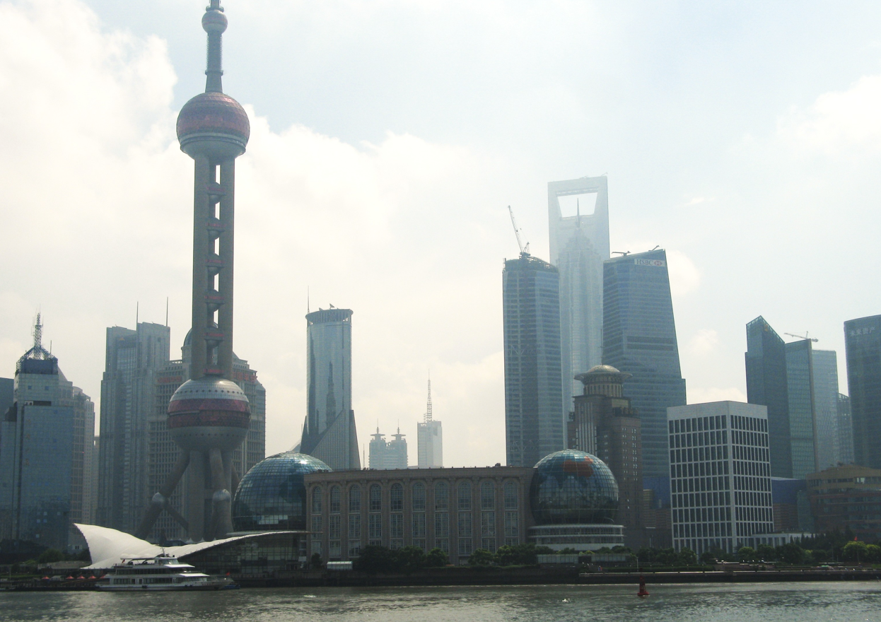 De skyline van Shanghai met de Oriental Pearl Tower en wolkenkrabbers tegen een bewolkte hemel.