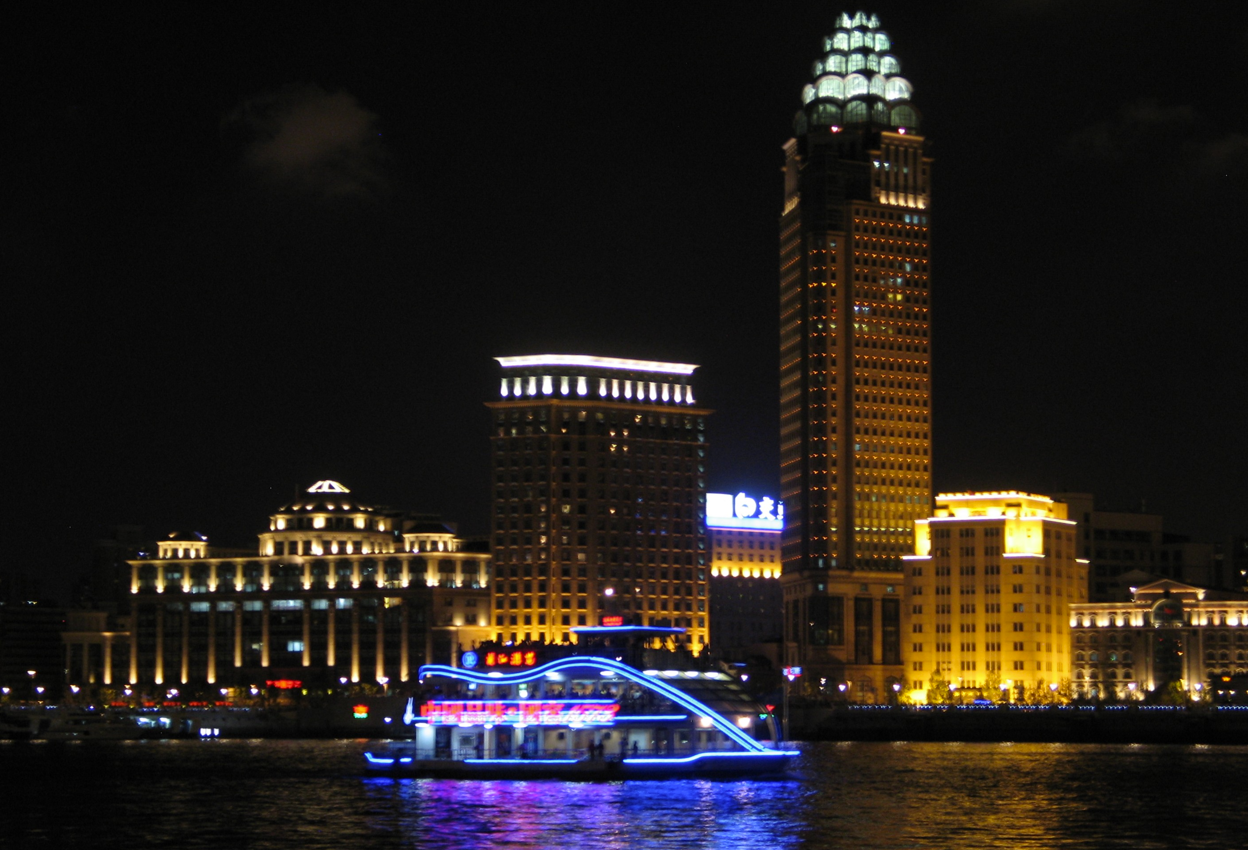 Nachtzicht op de skyline van Shanghai met verlichte gebouwen en een kleurrijke boot op het water.