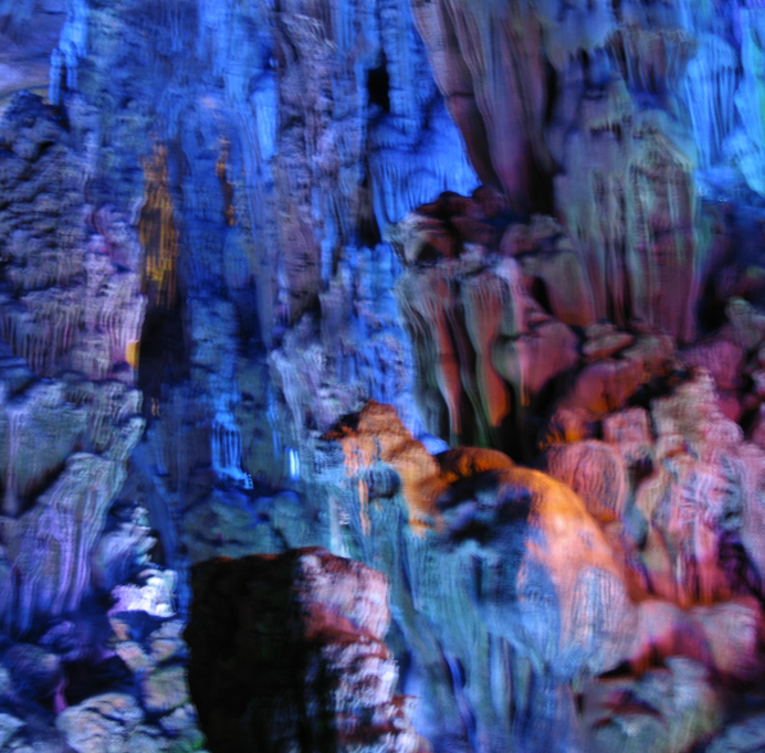 Het interieur van de grot wordt verlicht door blauwe, oranje en paarse lampen, waardoor de stalactieten en stalagmieten goed zichtbaar zijn.