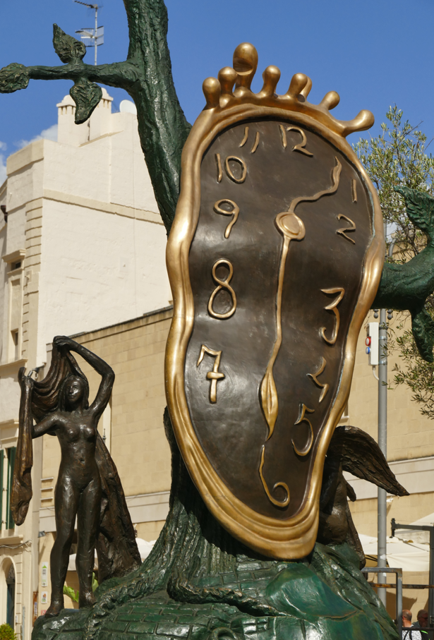 Bronzen beeld met een smeltende klok en figuren, voor een gebouw.