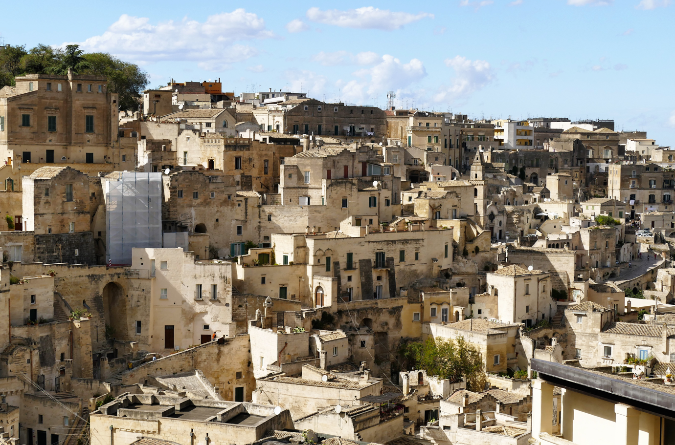 Dicht opeengepakte stenen gebouwen op een heuvel in Matera, Italië, onder een blauwe hemel.
