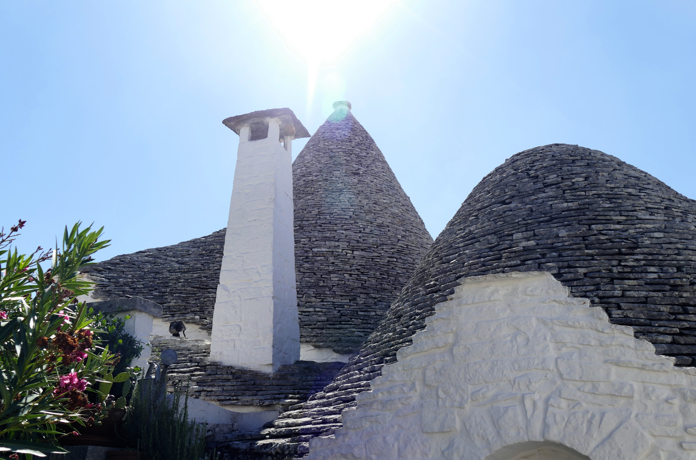 Witgekalkte trulli-gebouwen met kegelvormige daken en een schoorsteen steken af ​​tegen een helderblauwe hemel.