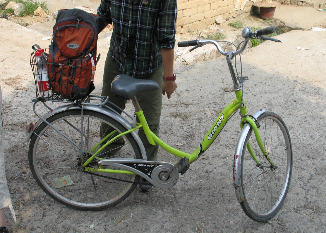 Een persoon staat naast een groene fiets met een rugzak op de bagagedrager.