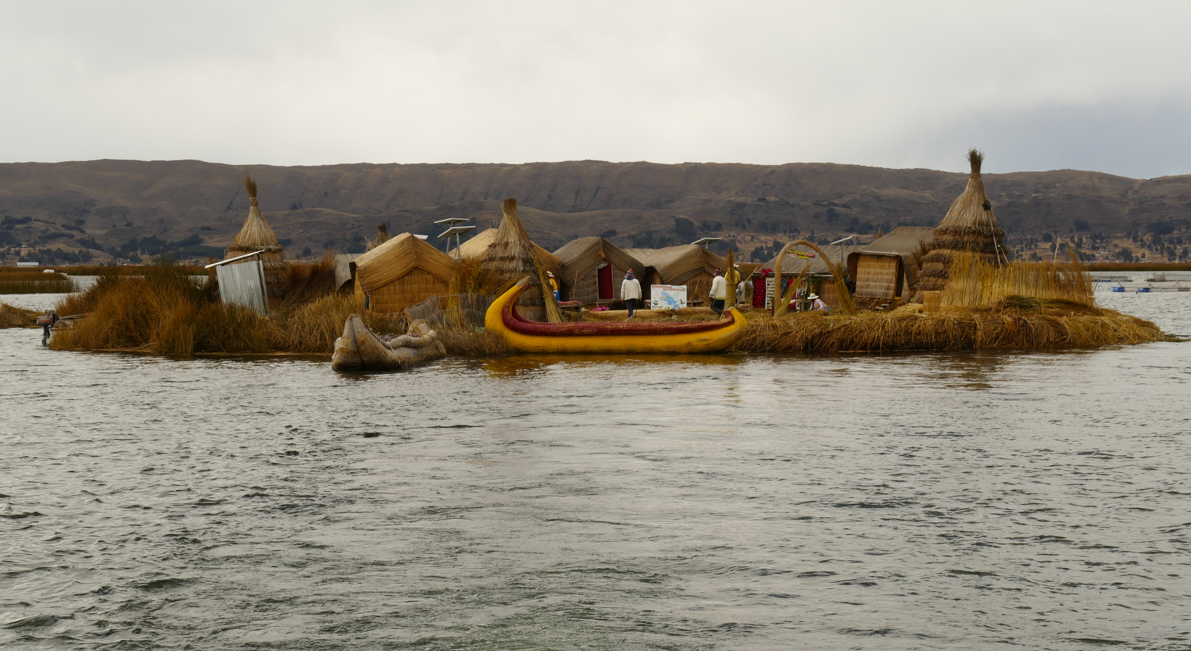 Drijvend eiland op een meer met rieten hutten en een gele boot. Op de achtergrond zijn bergen te zien.