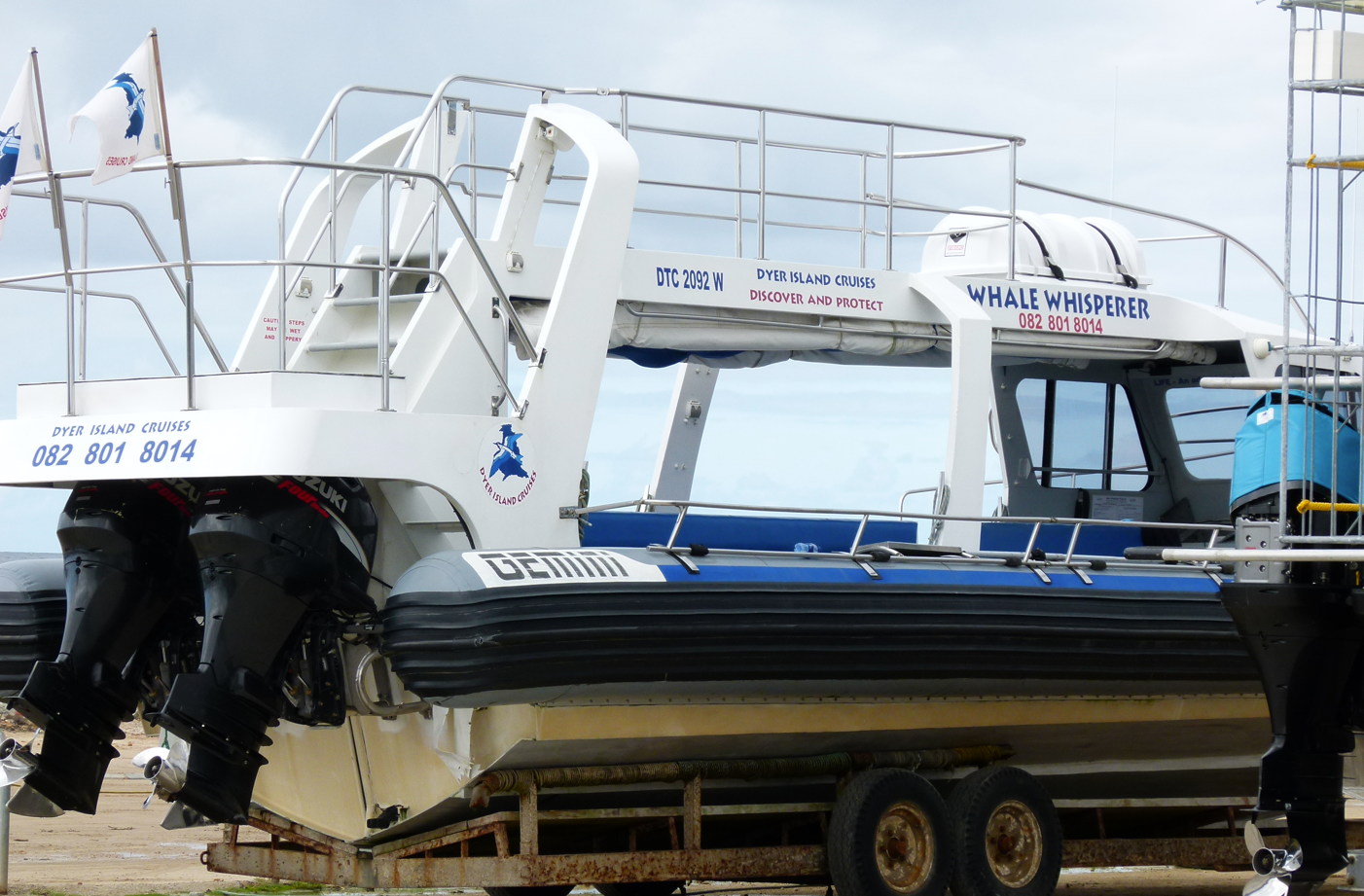 Witte en blauwe boot op trailer, meerdere buitenboordmotoren, Kings-logo, openlucht zitgedeelte.