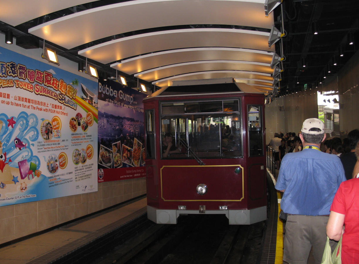 Een bordeauxrode tram op een station, met wachtende passagiers.