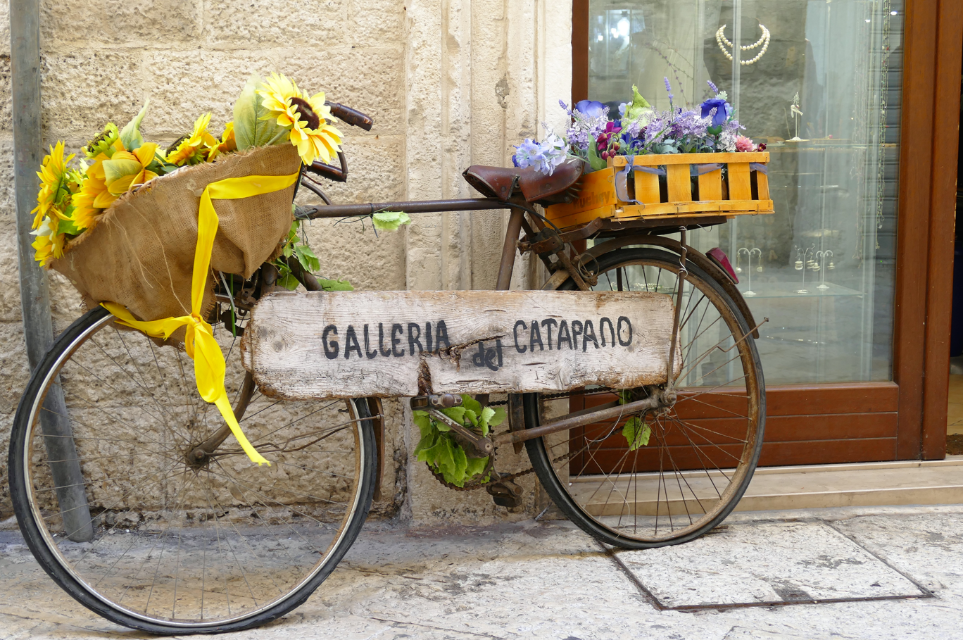 Een oude fiets versierd met bloemen en een bord met de tekst 