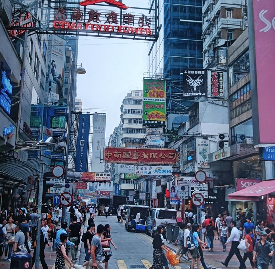 Een druk straatbeeld in Hongkong met voetgangers, reclameborden en hoge gebouwen.