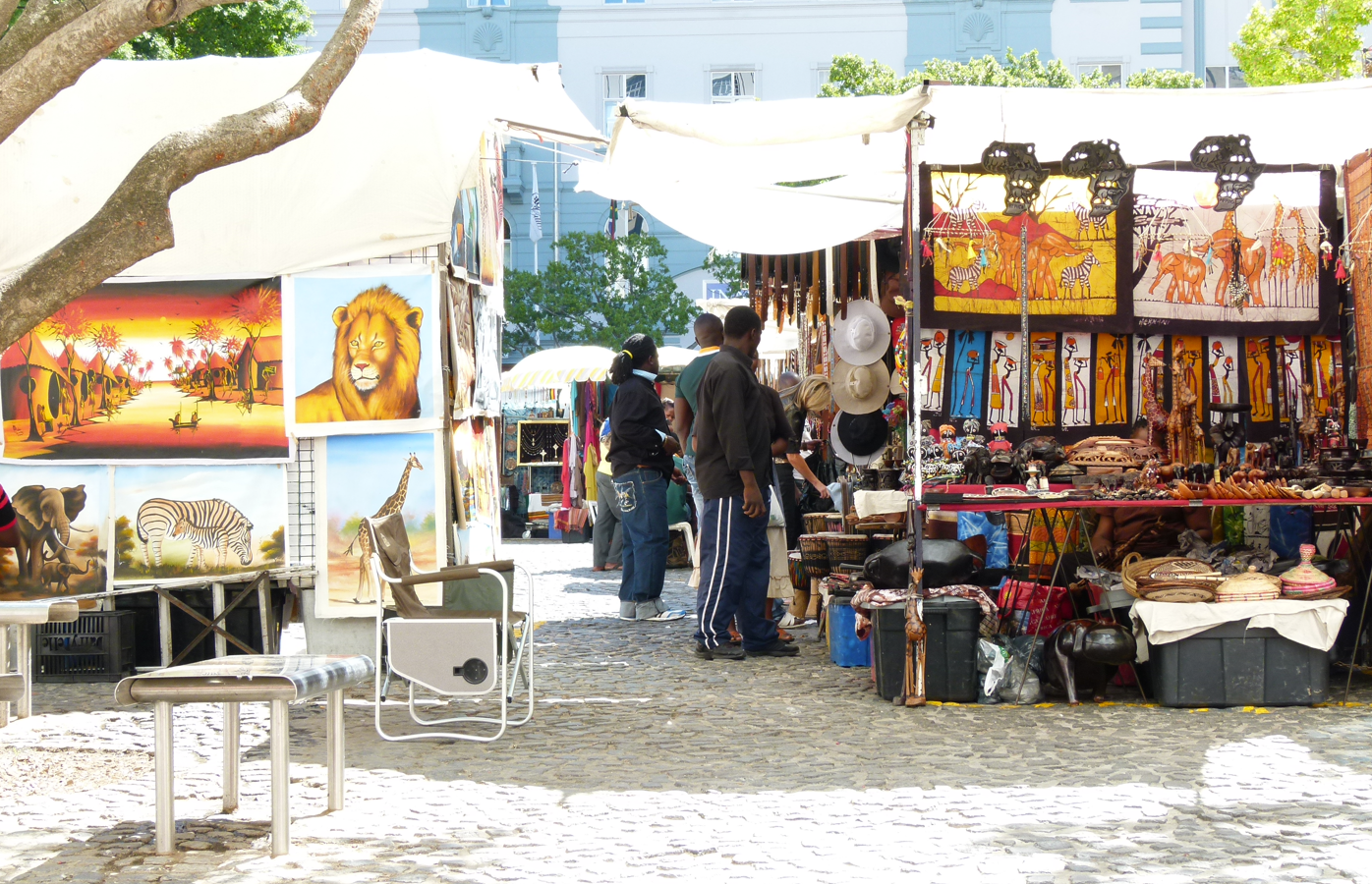 Marktstalletjes met kunst en handwerk. Mensen slenteren onder luifels op een straat met kinderkopjes.