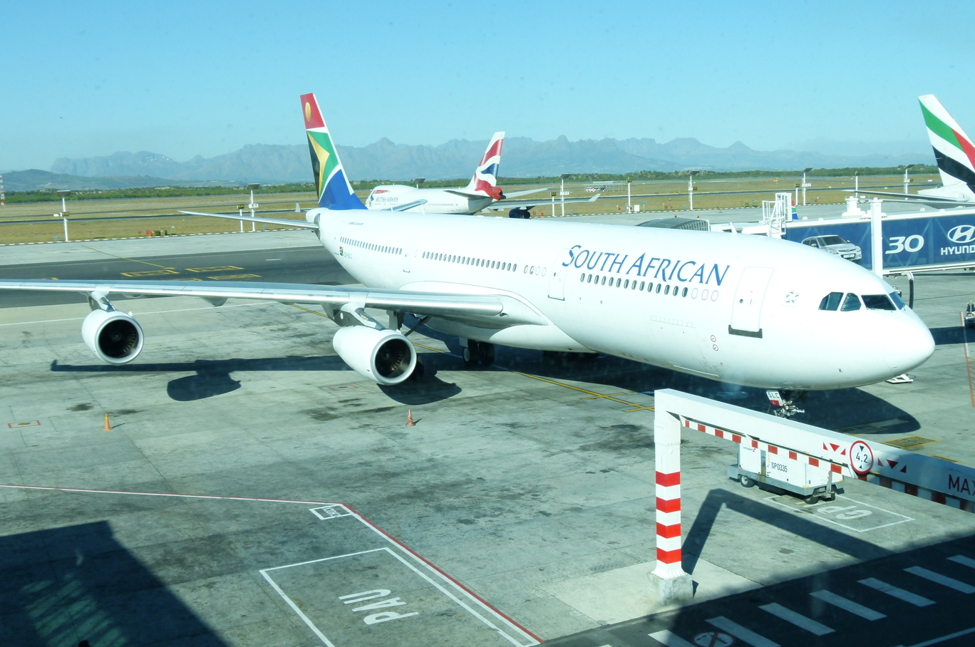 Een Airbus A340 van South African Airways staat geparkeerd bij een gate op een luchthaven op een zonnige dag.