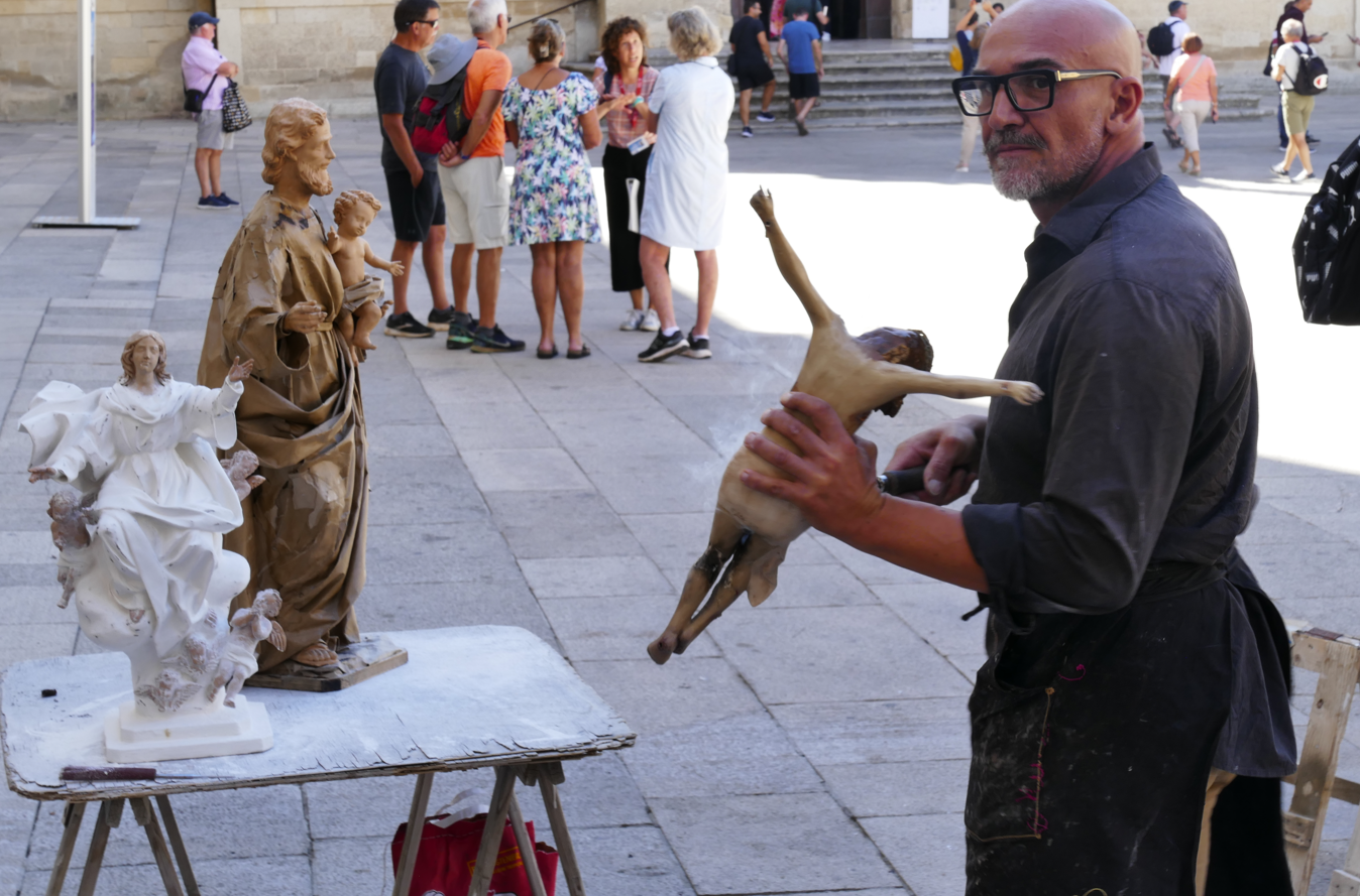 Een man houdt een sculptuur vast en poseert naast twee anderen, met een menigte mensen op de achtergrond.