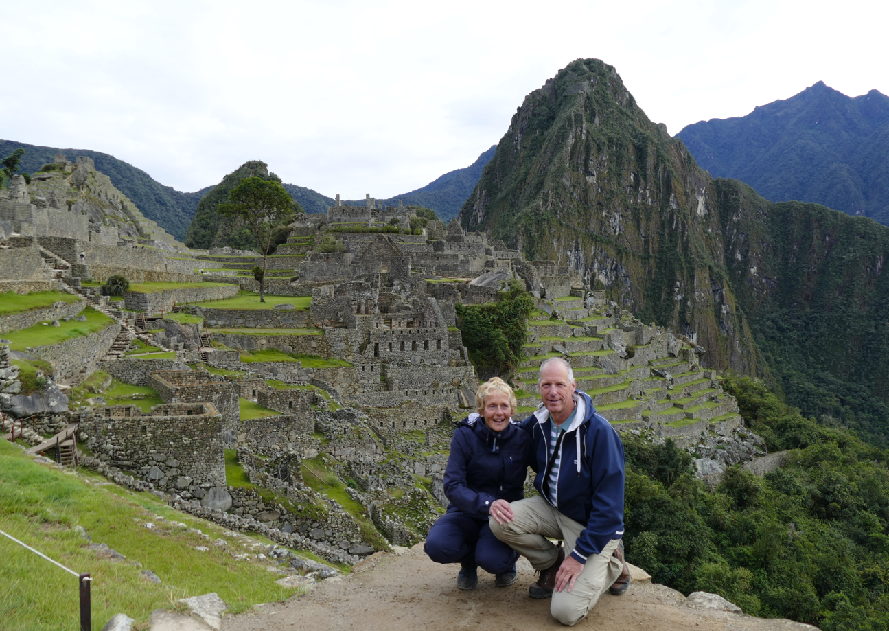 Een stel knielt bij Machu Picchu en poseert voor de oude ruïnes. Bewolkte lucht, weelderige bergen.