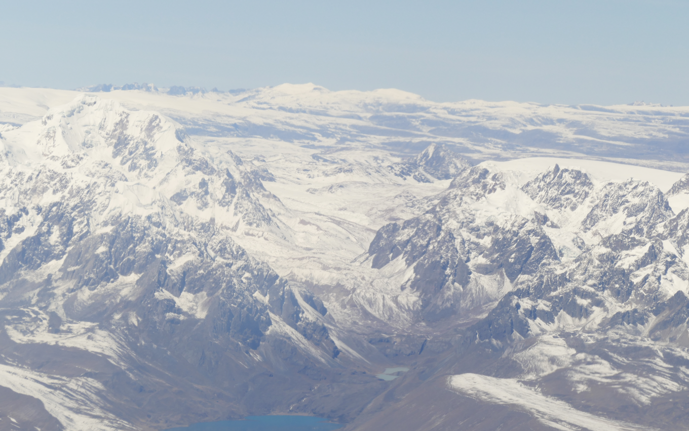 Besneeuwde bergen onder een helderblauwe hemel; enkele bergtoppen en een klein wateroppervlak zijn zichtbaar op de voorgrond.