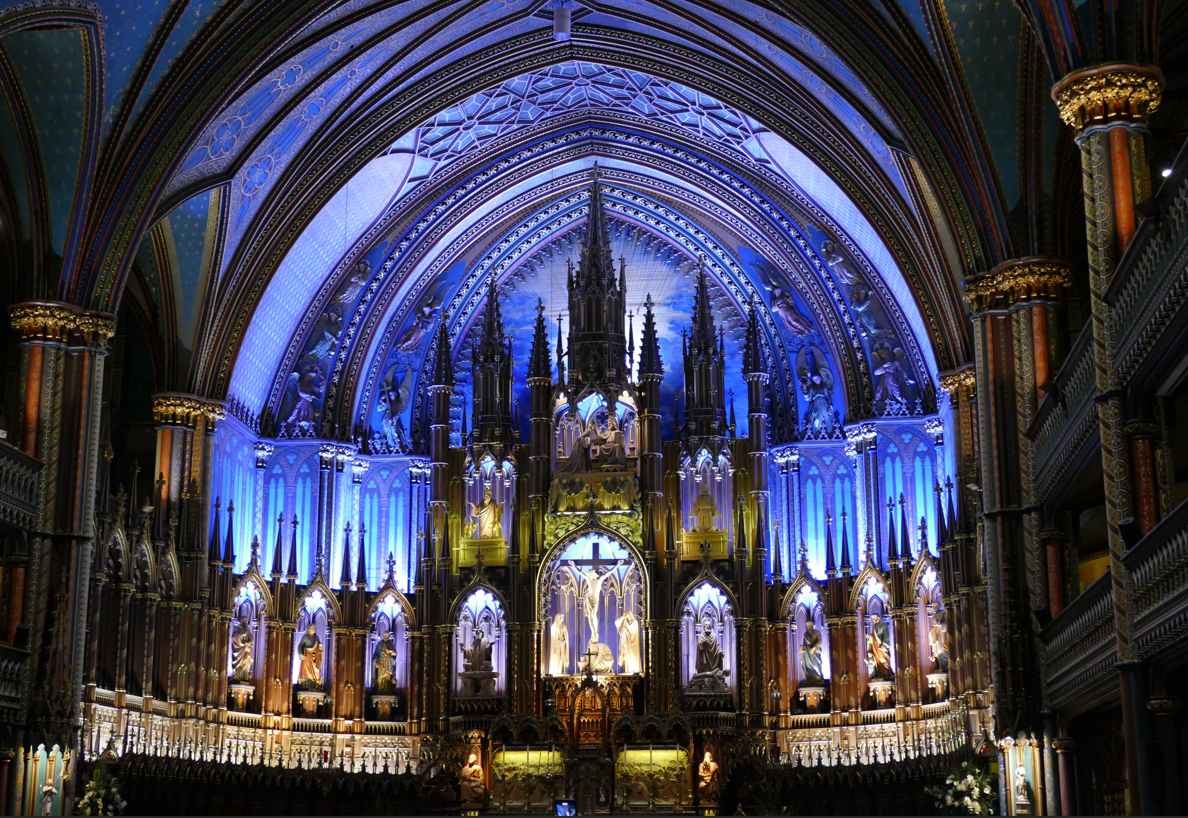 Interieur van een kathedraal met een blauw en goud verlicht altaar, sierlijke architectuur en een gewelfd plafond.