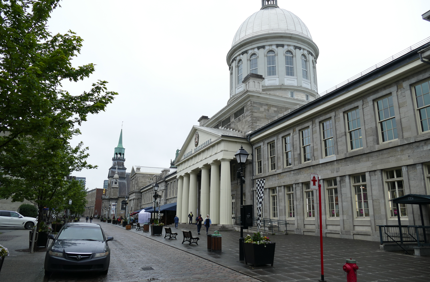 Straatbeeld van de Bonsecoursmarkt in Montreal, met een gebouw met een koepel en een lange constructie met zuilen.