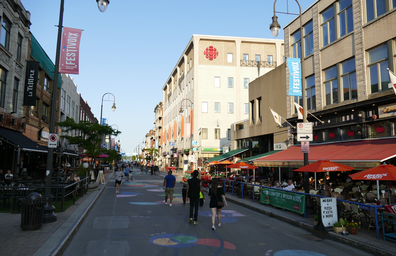 Straatbeeld met gebouwen, restaurants en mensen die op een zonnige dag wandelen.