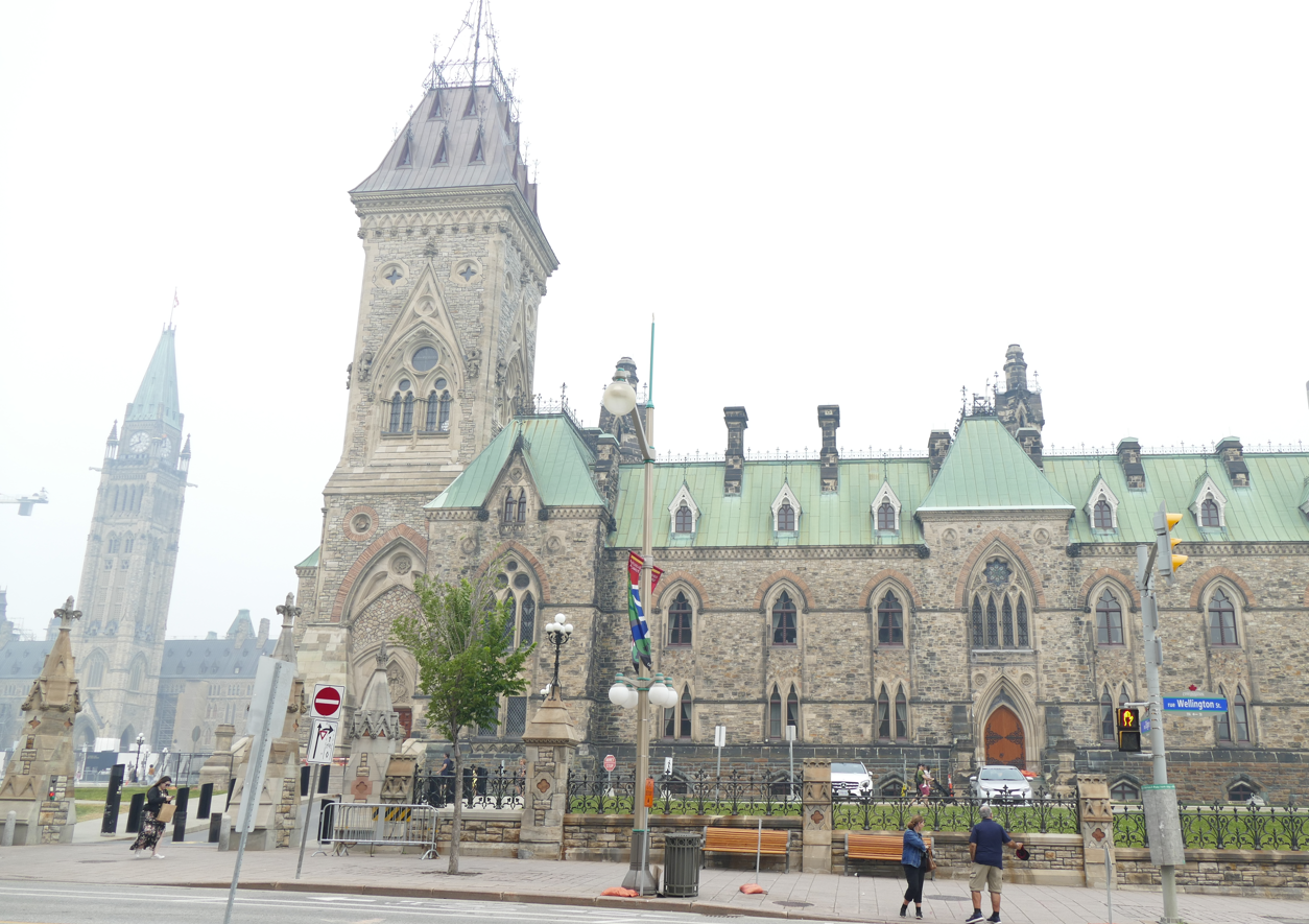 Parlementsgebouw, Ottawa, Canada. Gotische architectuur van steen onder een bewolkte hemel. Mensen lopen voorbij.