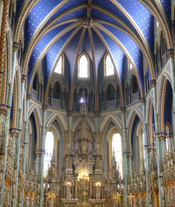 Interieur van een kerk met een blauw sterrenhemelplafond en een rijk versierd gouden altaar. Boogvensters en zuilen.