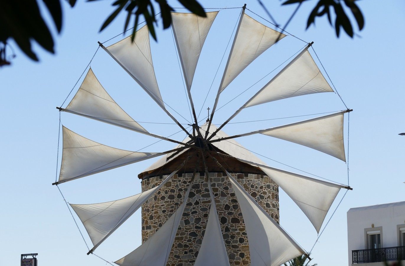 Een windmolen met witte wieken tegen een blauwe hemel, een stenen gebouw.