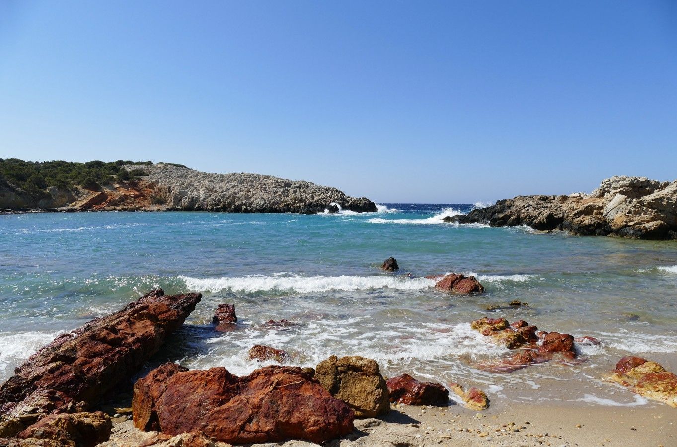 Rotsachtig strand met blauw water en een heldere hemel.