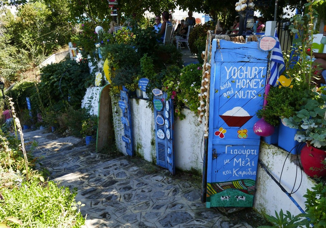 Stenen trappen leiden langs een blauw bord met de tekst 'yoghurt met honing en noten' in een kleurrijke buitenomgeving.