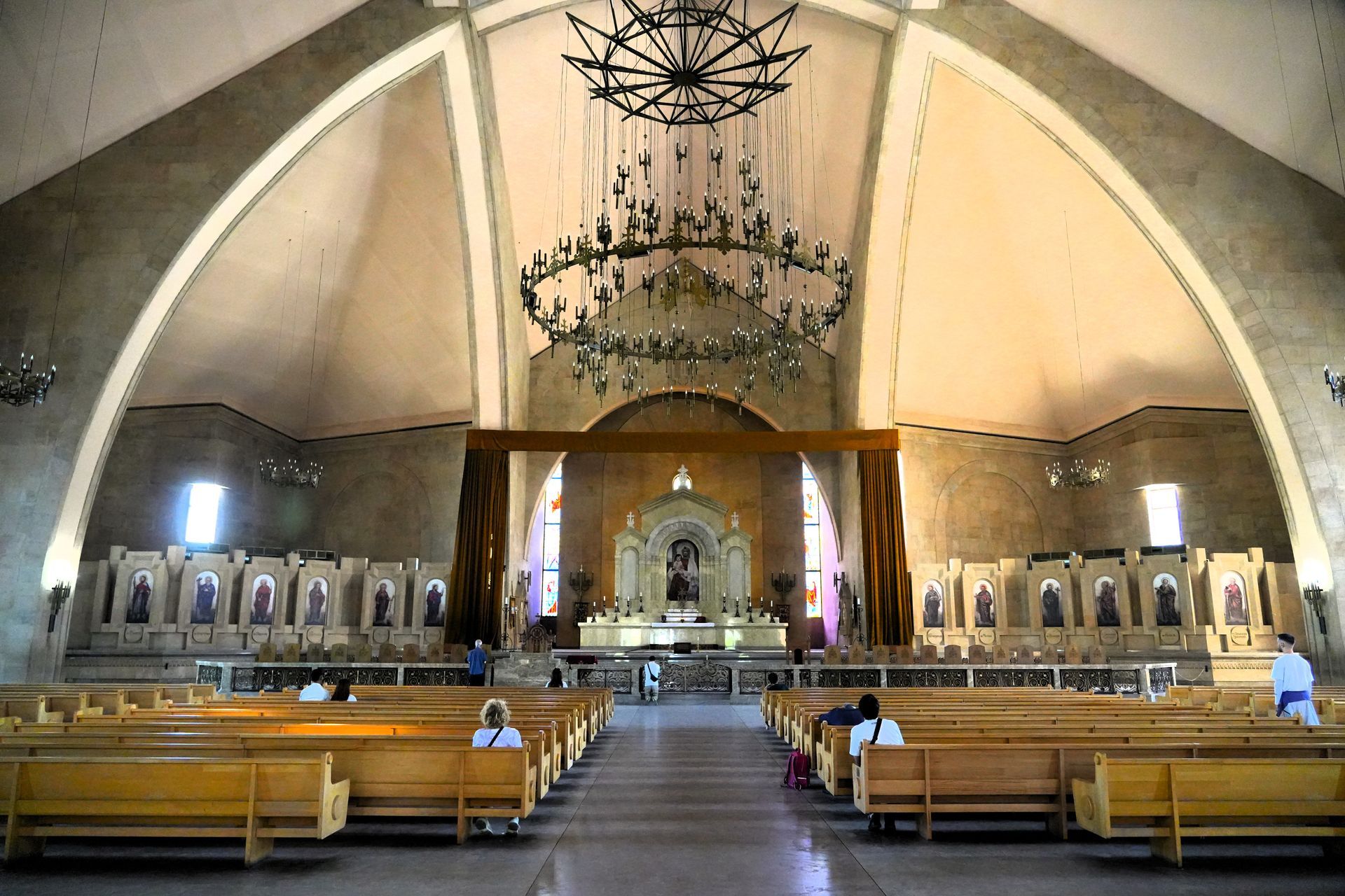 Interieur van een kerkzaal met kerkbanken, altaar en hangende kroonluchters onder een gewelfd plafond.