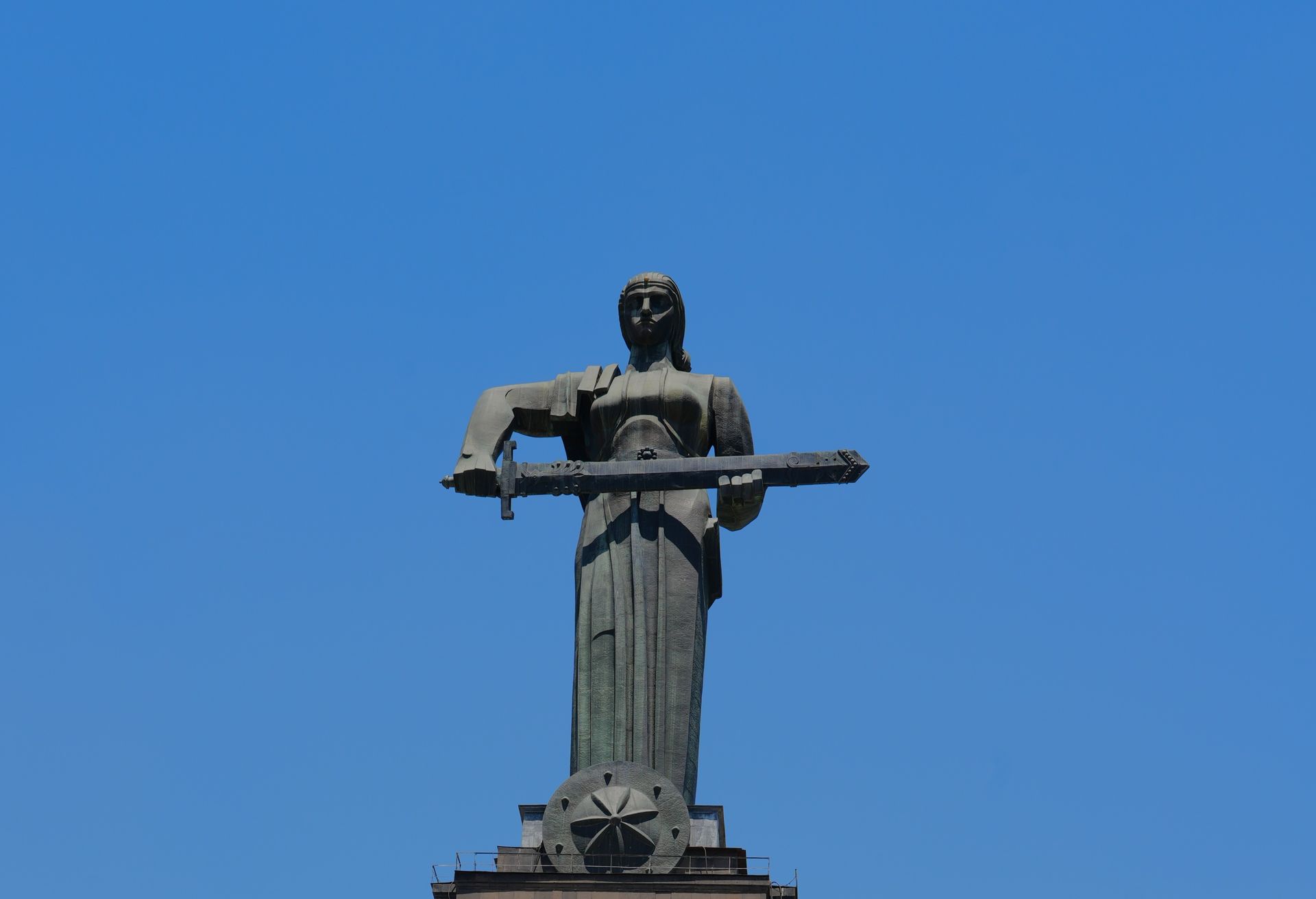 Standbeeld dat een horizontaal object vasthoudt tegen een helderblauwe hemel.