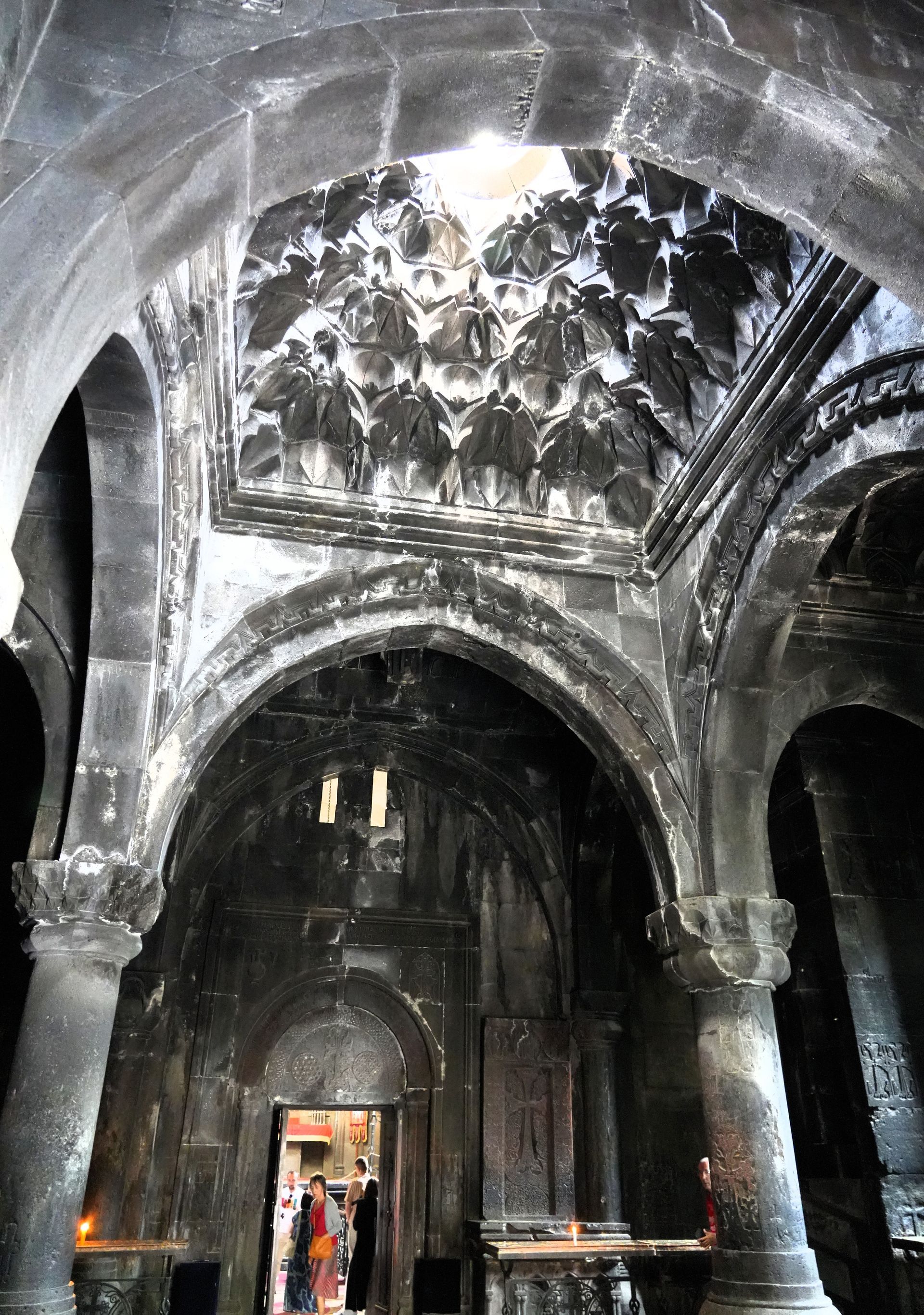 Het donkere stenen interieur van een kerk of kathedraal met gewelfd plafond, spaarzaam verlicht door een rijkversierd gewelf.