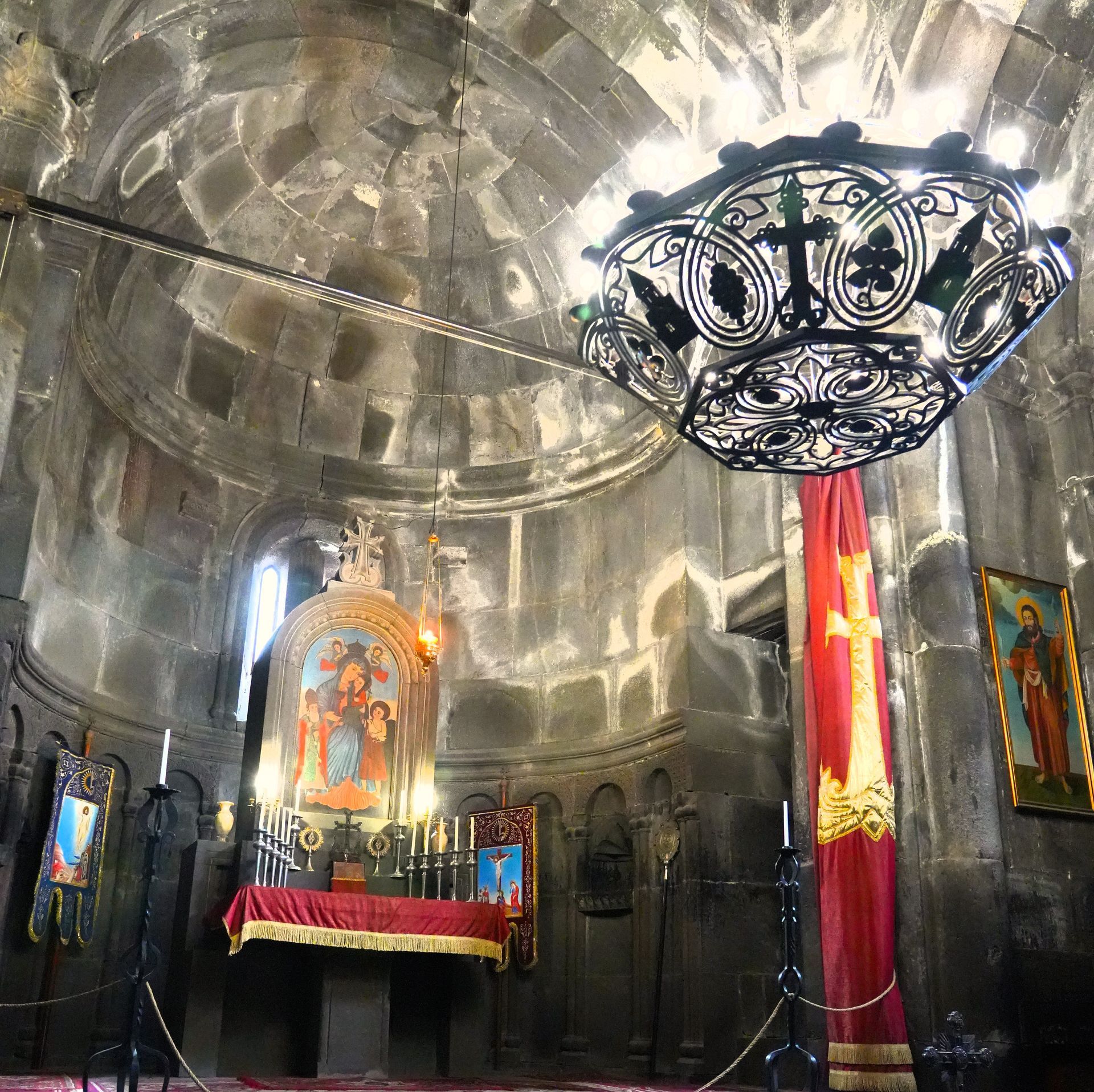 Rijk versierd kerkinterieur met stenen koepelplafond, iconenaltaar, rode gordijnen en hangende kroonluchter.