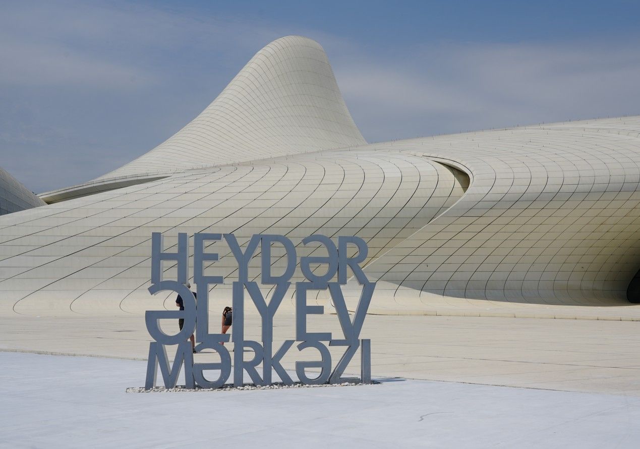 Abstract wit architectonisch landschap met blauwe metalen letters op de voorgrond tegen een bewolkte hemel.