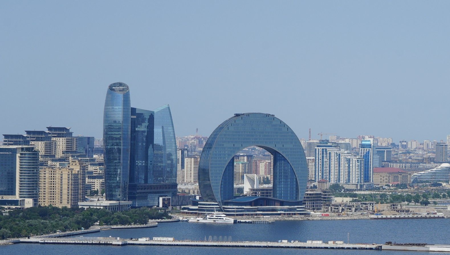 Moderne skyline aan het water met een opvallend ringvormig gebouw en hoge glazen torens.