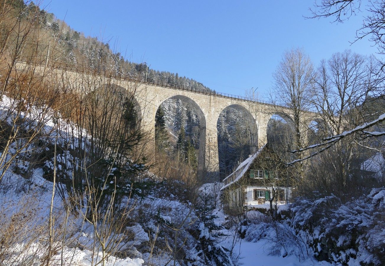 Een stenen boogbrug over een besneeuwd landschap met een huis eronder.