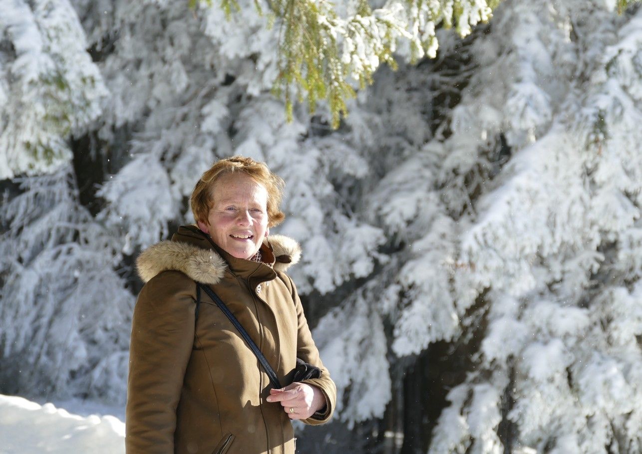 Vrouw in bruine jas glimlacht in een met sneeuw bedekt bos.