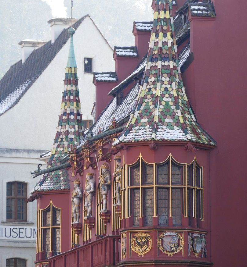 Rood gebouw met sierlijke erkers, beelden en torenspitsen met pannendak. In Freiburg, Duitsland.