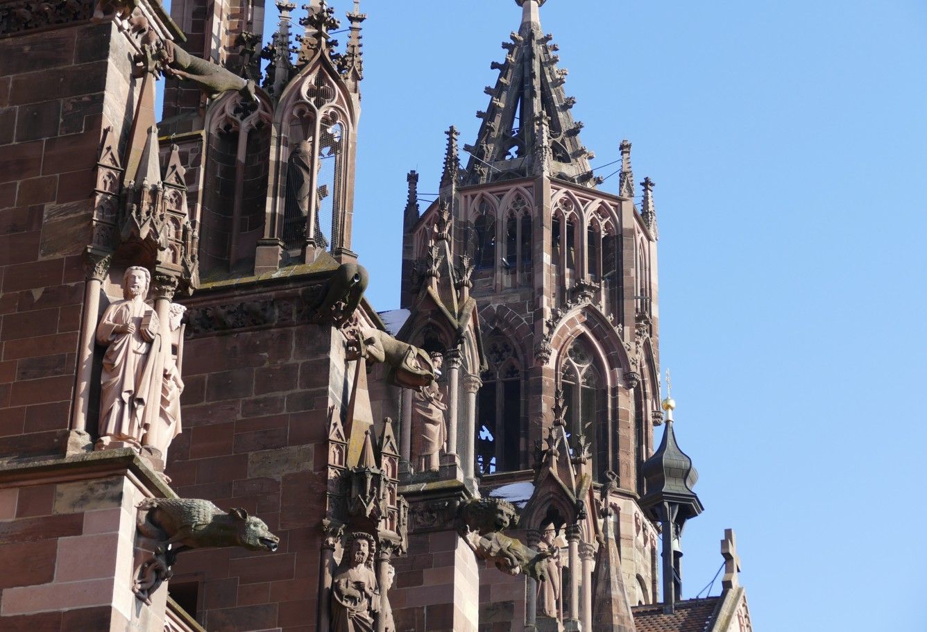 De buitenkant van een gotische kathedraal met sierlijke houtsnijwerken en spitse torenspitsen tegen een blauwe hemel.