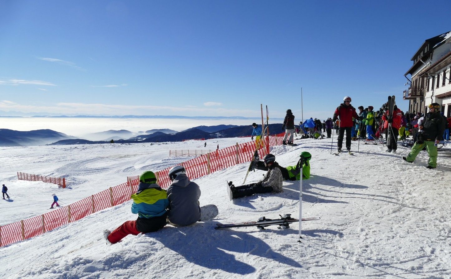 Mensen ontspannen en skiën op een met sneeuw bedekte berg onder een helderblauwe hemel.