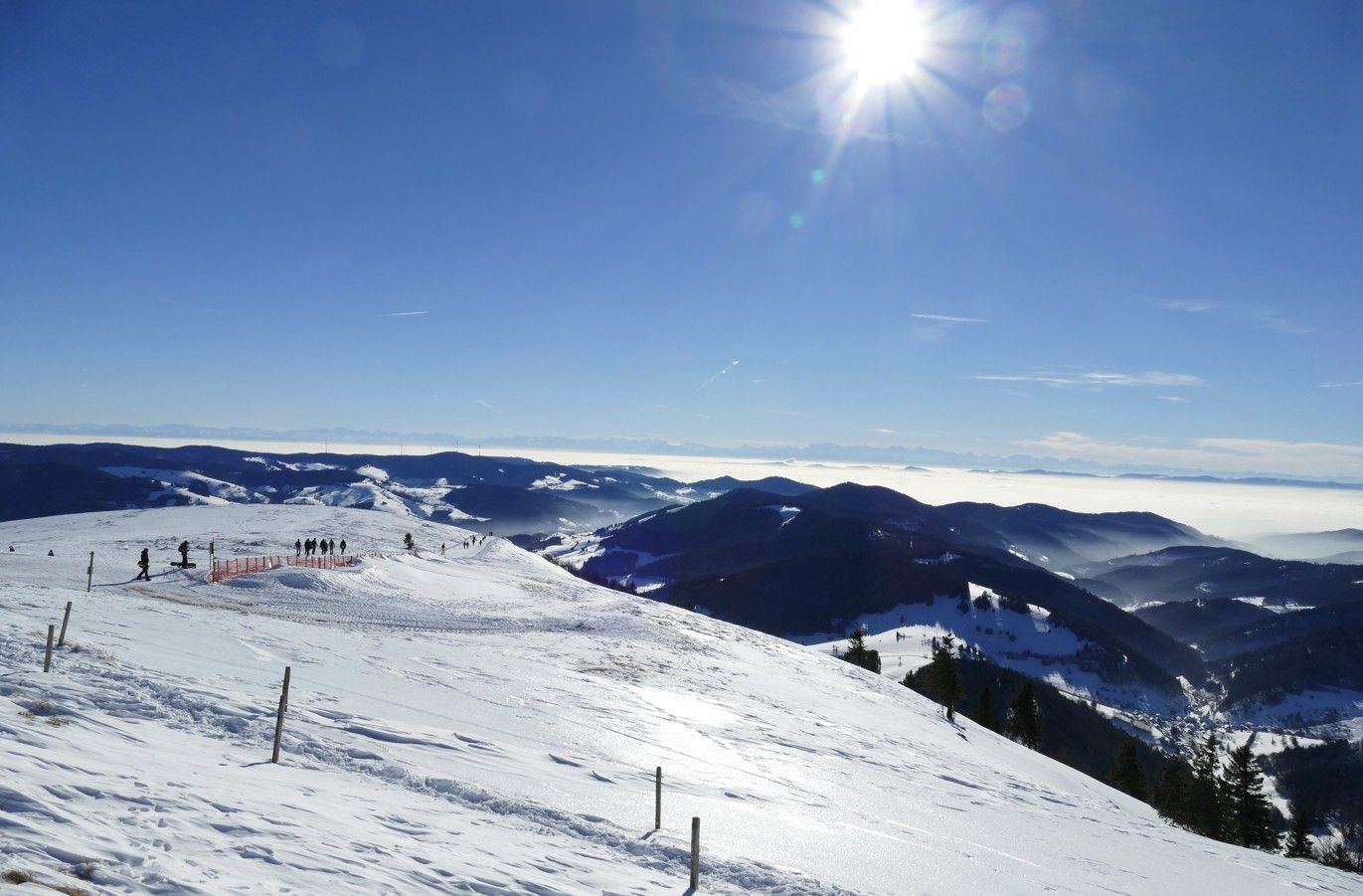 Besneeuwde bergkam met een stralende zon aan een helderblauwe hemel.