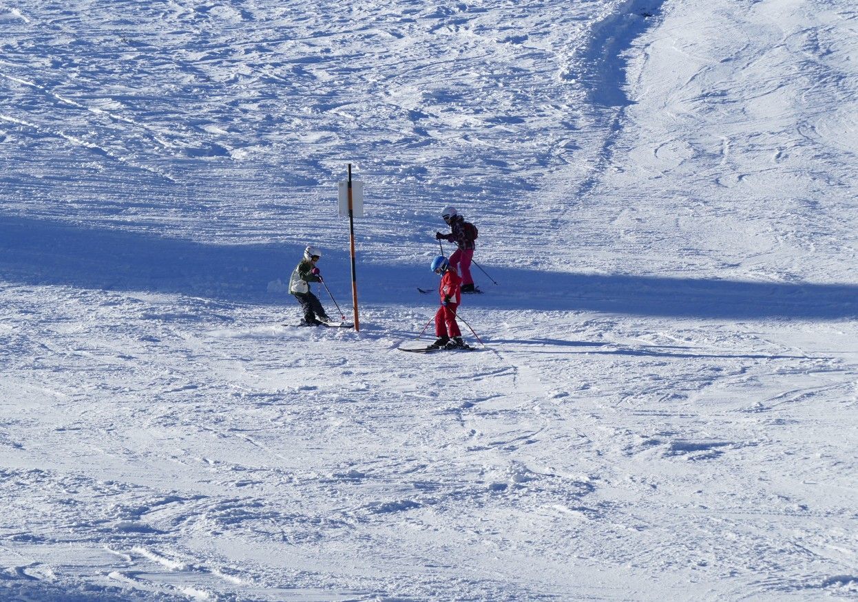 Een skiër in een rood pak en een kind op ski's bij een paal in een besneeuwd gebied.