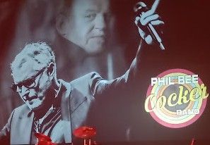 Zanger Joe Cocker treedt op het podium op, met een microfoon in zijn hand waarop een afbeelding van zijn gezicht .