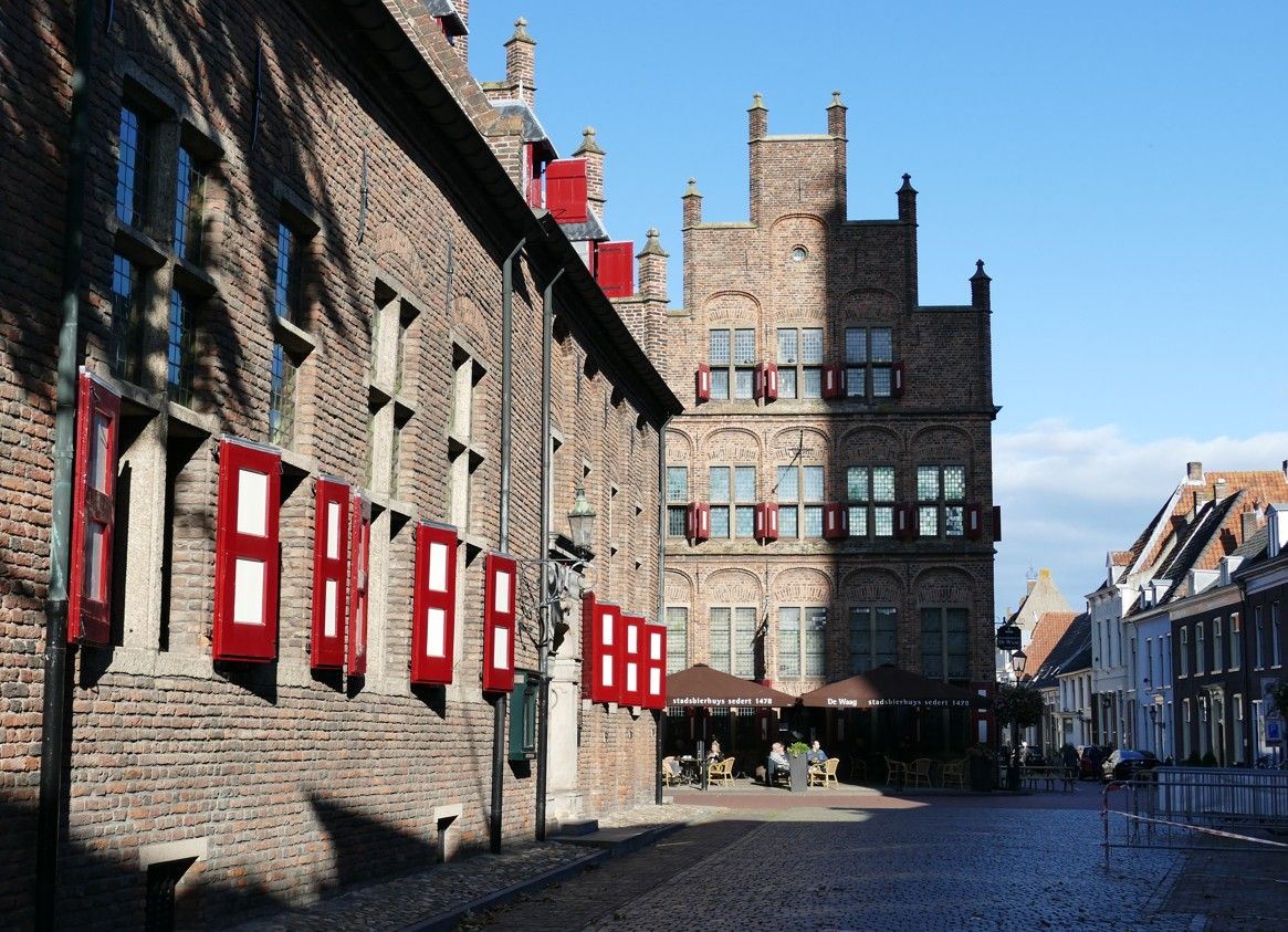 Bakstenen gebouwen met rode luiken, in een zonovergoten straat met kinderkopjes.