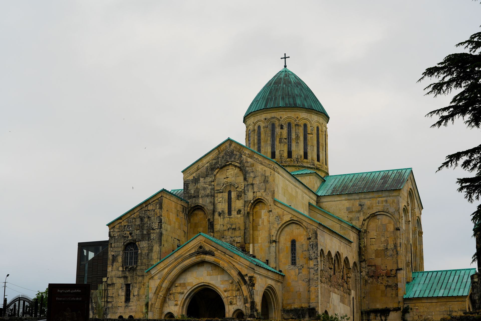 Stenen kerk met turquoise koepels en een kruis tegen een bewolkte hemel.