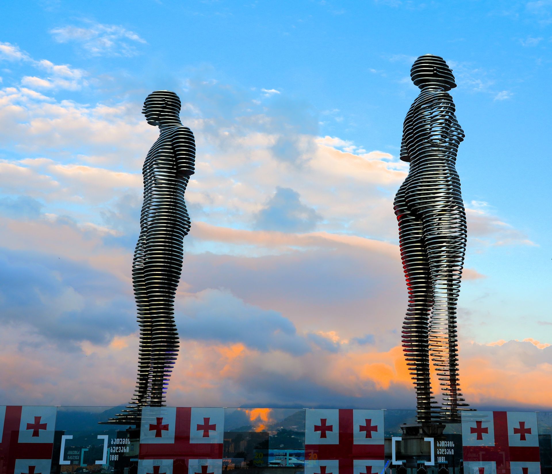 Twee hoge spiraalvormige metalen sculpturen tegen een zonsondergang, met daaronder vakjes met de Zwitserse vlag.