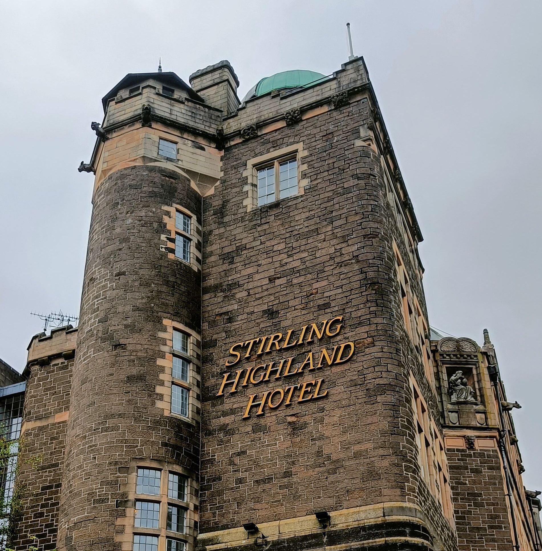 Stirling Highland Hotel, een stenen gebouw met een toren en gouden letters.